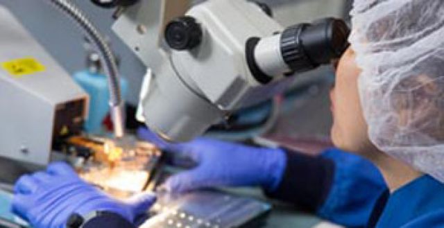 A scientist looks through a microscope in a lab.
